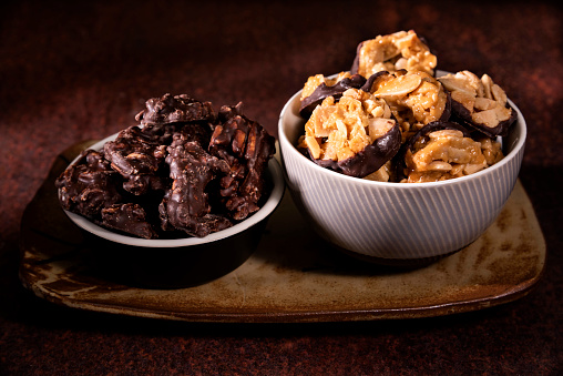 A bowl of Chocolate Florentines cookies beside chocolate and almond treats. These are placed on a ceramic plate against a dark background.