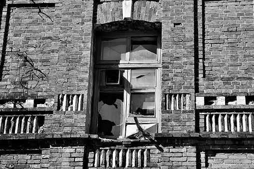A black-and-white photo of an abandoned brick building and a broken window. Old buildings and abandoned buildings in Vladivostok. Brick ruins in Vladivostok.