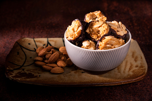 A bowl of Chocolate Florentines cookies beside whole almonds. These are placed on a ceramic plate.