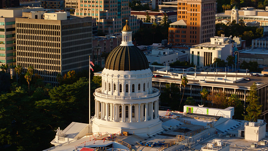 Drone shot of the California State Capitol amid downtown office buildings in Sacramento at sunset. \n\nAuthorization was obtained from the FAA for this operation in restricted airspace.