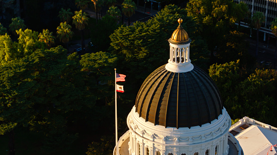 Drone shot of the California State Capitol amid downtown office buildings in Sacramento at sunset. \n\nAuthorization was obtained from the FAA for this operation in restricted airspace.