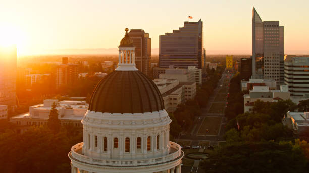 drone shot do capitólio do estado da califórnia com pôr do sol e ponte torre à distância - building exterior sacramento county california state capitol building - fotografias e filmes do acervo