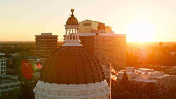 drone shot of us and ca flags flying over california state capitol with dramatic lens flare - building exterior sacramento county california state capitol building - fotografias e filmes do acervo