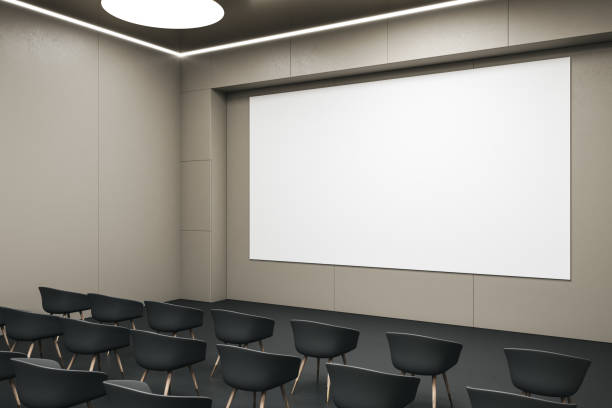 istock Perspective view on blank white wall board with space for your logo or text on light beige wall in empty auditorium in front of black chairs. 3D rendering, mockup 1435109044