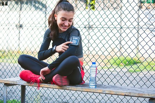 Portrait of a smiling teenage girl doing sports in the city. Monitoring progress on a mobile phone. Sport and healthy active lifestyle concept. Technology and sport.
