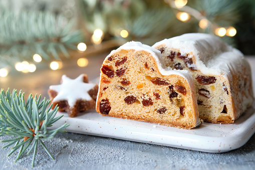 Christmas stollen on festive background with garland, Xmas lights. Traditional German dessert for Christmas celebration. Traditional German fruit cake.