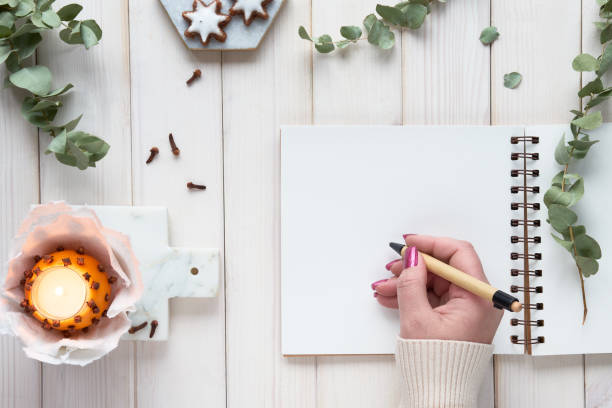 istock Wintertime notebook mockup with eucalyptus twigs, natural orange tea light with cloves and gingerbread cookies on ceramic board. Flat lay, top view on off white rustic wooden ff white planks. 1435114979
