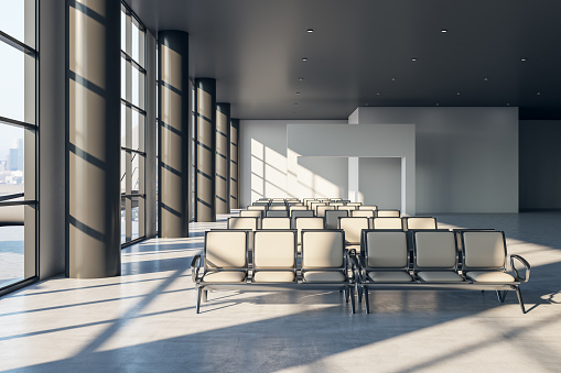 Front view on stylish airport seats in sunlit empty waiting area hall with big panoramic windows and concrete floor. 3D rendering