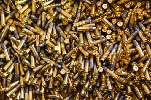 Large heap of black and golden small-caliber bullets on white table at bright light in production plant workshop extreme closeup