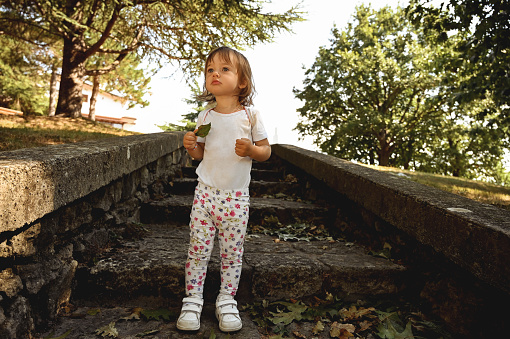 cute toddler child standing in an autumn park alone and lookinf away.