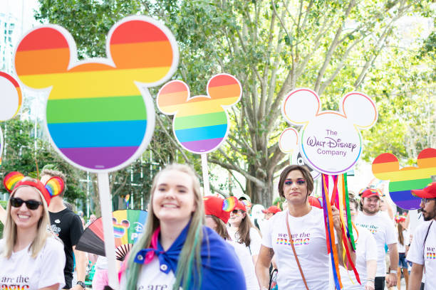 Woman with a sign and Group of members of the LGBTIQIA+ And Allied Employees of The Walt Disney Company in the Come Out With Pride Orlando parade 2022 Orlando, Florida. October 15, 2022. Woman with a sign and Group of members of the LGBTIQIA+ And Allied Employees of The Walt Disney Company in the Come Out With Pride Orlando parade on the E Central Blvd street. disney world stock pictures, royalty-free photos & images