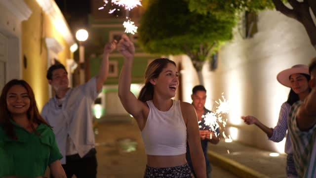 Young woman and her friends playing with sparklers in the city at night