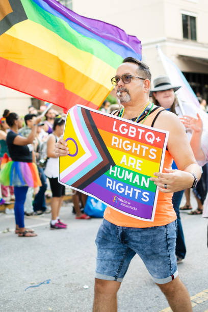 homem membro do rainbow democrats com um sinal de direitos lgbtq+ são direitos humanos, e bandeira lgbt, na parada come out with pride orlando 2022 - pulse orlando night club & ultra lounge - fotografias e filmes do acervo