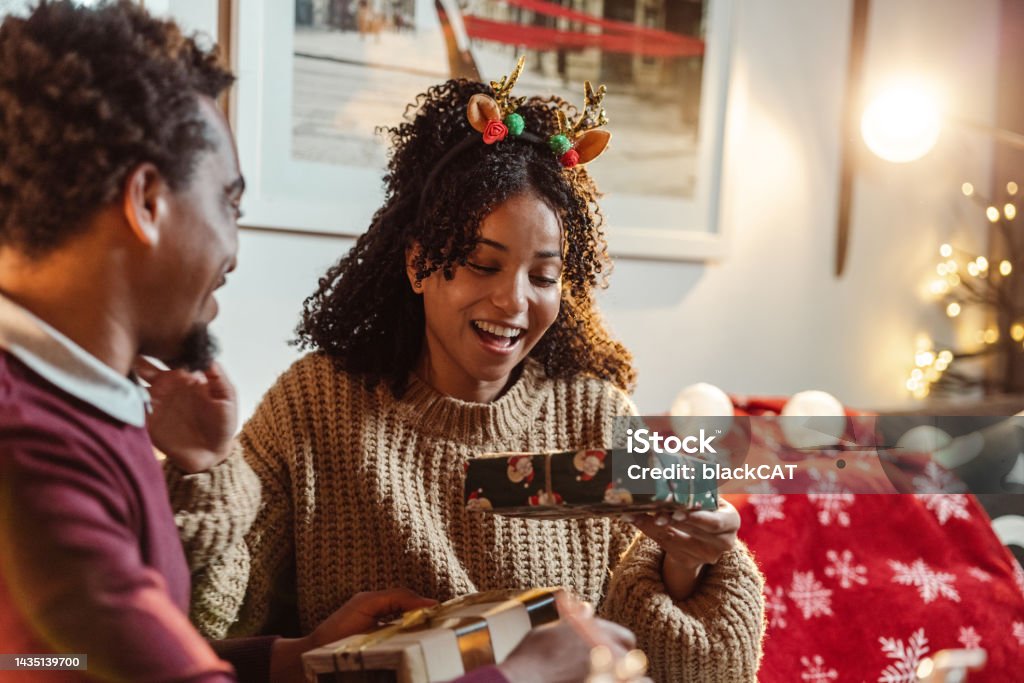 Christmas gift exchange at home Happy young African-American couple enjoying at home during winter holidays Christmas Present Stock Photo