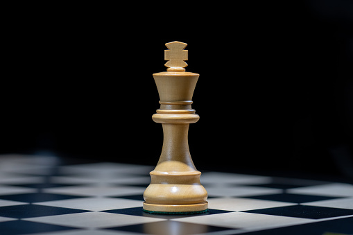 Close-up view of alone wooden king piece on chessboard against black background. Strategy, risk management and leadership concept.