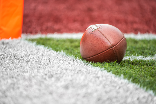 A low angle view of a leather American Football spotted next to a white side line within a yard of the end zone.