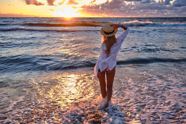 carefree woman in straw hat posing in the sunset on the sea beach. Vitality healthy living concept. Girl in pareo on sunset at stormy sea.