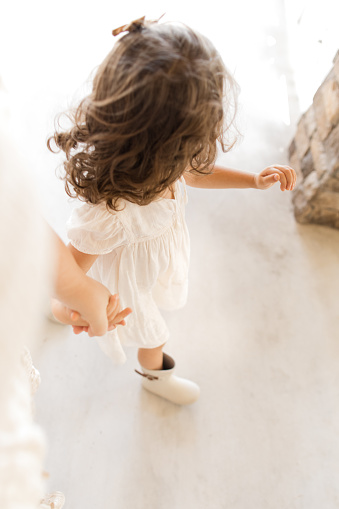 A 3-Year-Old Toddler Girl Wearing a White Dress, A Brown Hair Bow & White Rain Boots on a White Country Porch