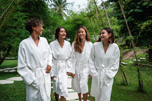 Smiling women are walking in bathrobes to the sauna through the green yard.
