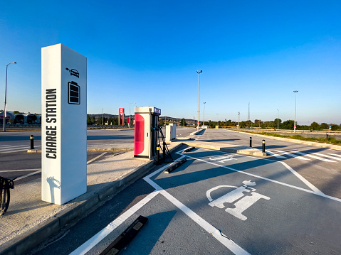 Modern outdoor electric quick car charging station for public at highway on sunny day with clear blue sky. Power supply for E-vehicle (EV). Automotive sign on asphalt.