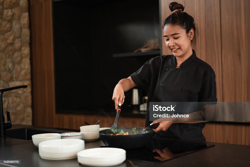 Chef preparing dinner in the kitchen Smiling, female chef is preparing a meal in the kitchen of a luxury villa. Chef Stock Photo