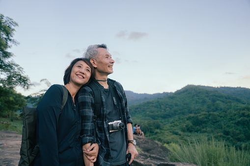 Happy Asian couple hikers on top of the mountain enjoying sunset over the tropical valley.