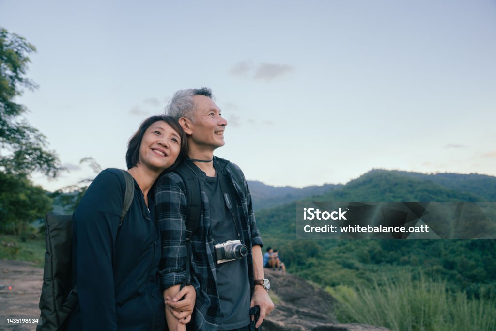 This is my life. Happy Asian couple hikers on top of the mountain enjoying sunset over the tropical valley. Couple - Relationship Stock Photo