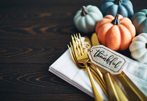 Thanksgiving background with pumpkins and gold cutlery wrapped with a gift tag reading THANKFUL