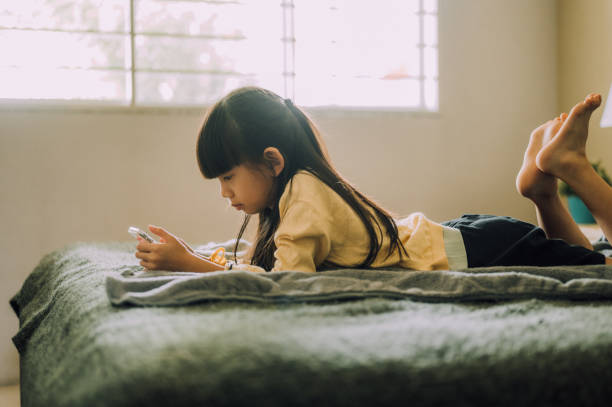 8세 여학생은 침대에 누워 휴대폰을 보고, 방과 후 스마트폰의 모바일 앱에서 문자 메시지를 보냅니다. - female 8 9 years child excitement 뉴스 사진 이미지