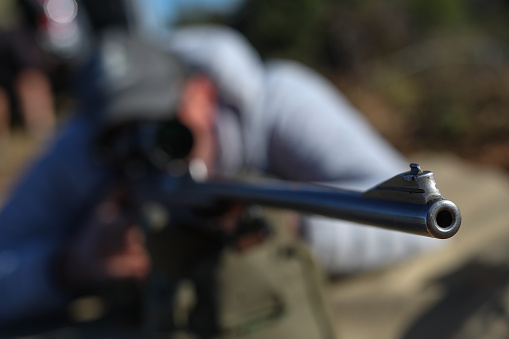 A barrell of a hunting rifle in focus with the hunter out of focus