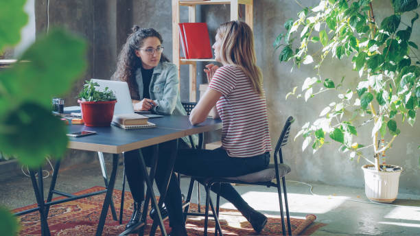 istock Young enterpreneurs are duscussing advertising strategy while sitting at table in modern office. Women are talking and gesturing, one of them is making notes. 1435220677