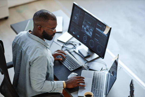 African American Software Developer Minimal high angle view at African American software developer working with computers and data systems in office desktop pc stock pictures, royalty-free photos & images