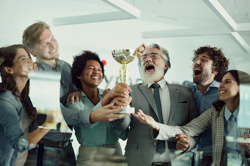 Group of cheerful entrepreneurs having fun while celebrating a trophy in the office. The view is through glass.