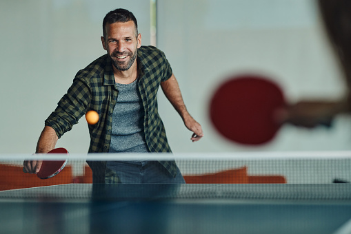 Happy man having fun while playing table tennis with his friend.