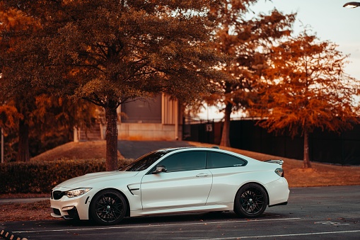 Tuscaloosa, United States – October 10, 2022: A white BMW M4 parked on a street with trees in the background