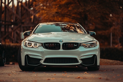 Tuscaloosa, United States – October 10, 2022: The front of a white BMW M4 parked on a street with trees in the background