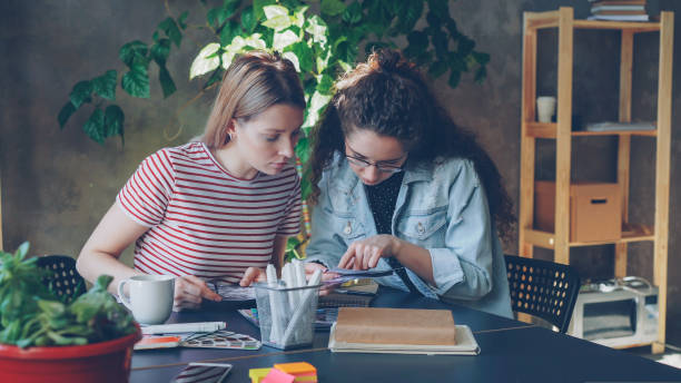 istock Young creative designers are looking at photos attentively and discussing them while sitting together at table. 1435226509