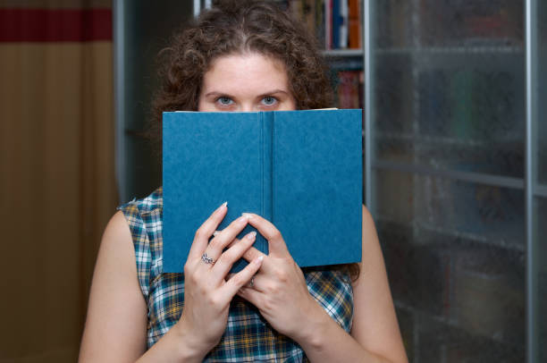 istock Woman reading a book standing by a bookcase 1435228104