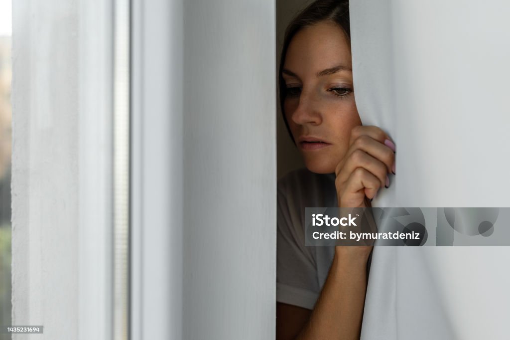 Woman scared looking through the window seeking safety Stalker - Person Stock Photo
