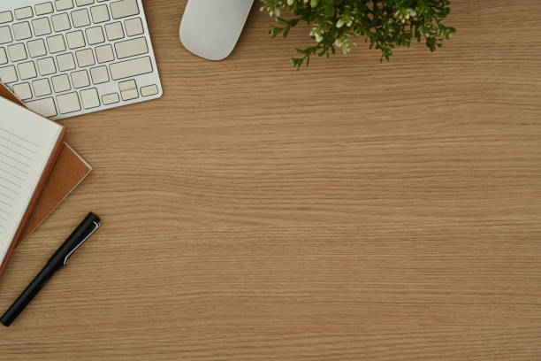 Wooden working desk with wireless keyboard, notebook, mouse and potted plant. Top view with copy space.