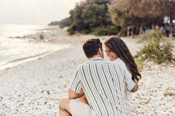 Happy couple talking while relaxing on a rocky beach.
