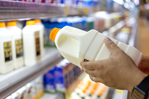 Close up of a man's hand picking up a bottle of organic fresh milk from the dairy aisle in supermarket. Healthy eating lifestyle and routine.