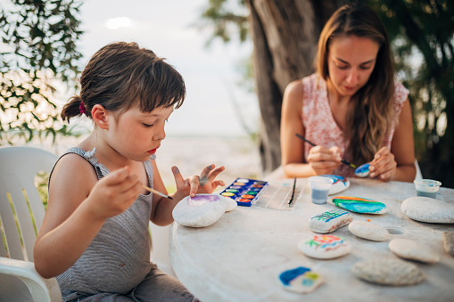 Mother and her cute little daughter use different water colors while having fun and drawing on rocks