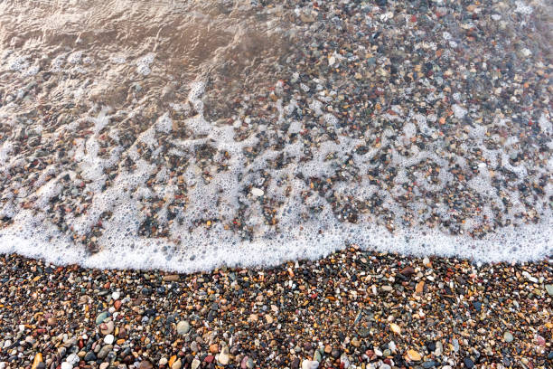 Natural stones amber yellow colored on beige sand ans sea wave. Aesthetic minimal nature scene with pebble stones on sandy background. Summer vacation or relaxation concept, selective focus, copyspace