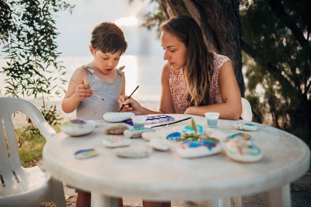 istock During sunset, mother and daughter sit at a table and paint on stones using water colors 1435235676