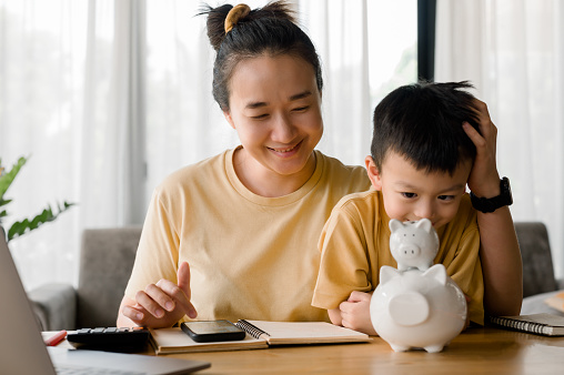 Family saving money concept, Asian Woman and son note family expenditures for a plan to spend the future in earnest, family and financial concept, finance and saving, save money. Family budget plan.