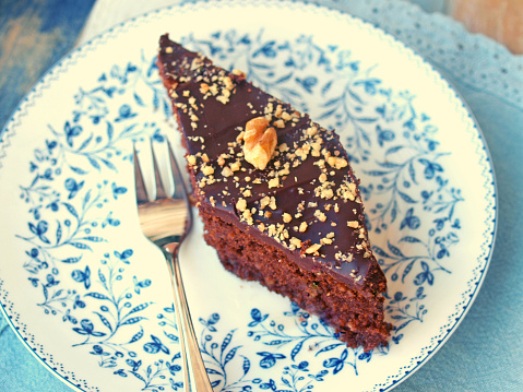 A piece of chocolate walnut cake on a plate decorated with ground walnuts