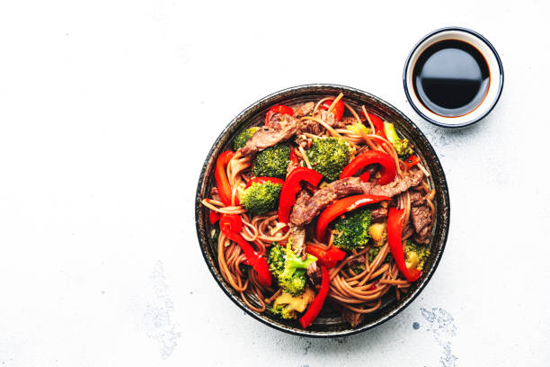 Stir fry noodles with vegetables and beef, paprika and broccoli with sesame seeds in  bowl on white table background, top view stock photo
