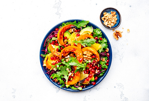 Fresh autumn pumpkin salad with baked pumpkin slices, red cabbage, avocado, arugula, pomegranate seeds and walnuts. Healthy vegan, vegetarian eating, comfort food. White background. Top view
