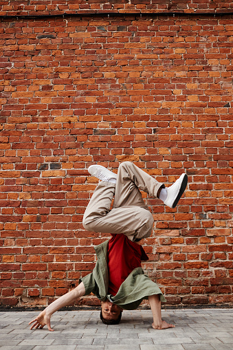 Vertical shot of young man doing breakdance headstand pose against brick wall, copy space